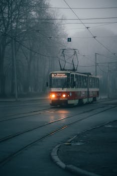 A nostalgic tram rides through a foggy city street creating an old-world atmosphere.