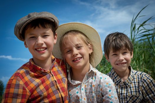 Three smiling children in vintage attire enjoying a sunny day outdoors.