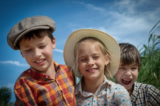 Three smiling children enjoying a sunny day outdoors in vintage attire. Capturing joy and friendship.