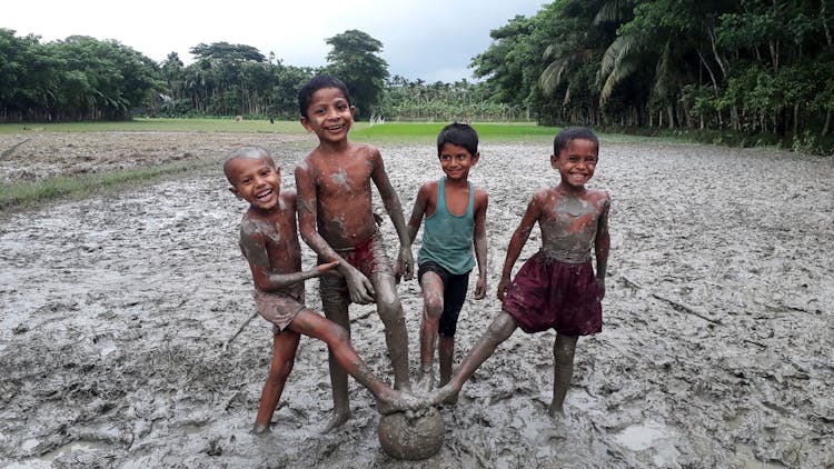 A Group Of Kids Playing In The Gray Mud 