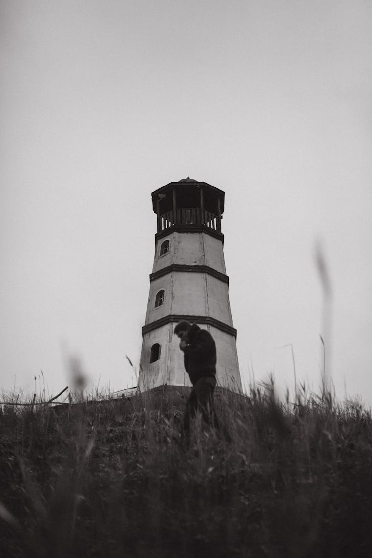 Man Walking In Field Near Lighthouse