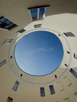 Perspective view through a circular architectural space towards a clear blue sky.