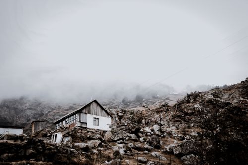 Free A solitary house nestled among rocks with a foggy mountain backdrop, creating a moody atmosphere. Stock Photo