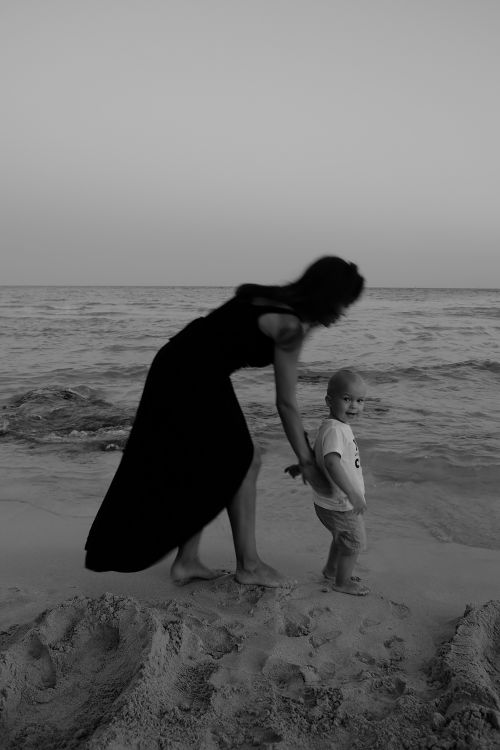 Free A black-and-white image of a mother and son walking on a beach. Stock Photo