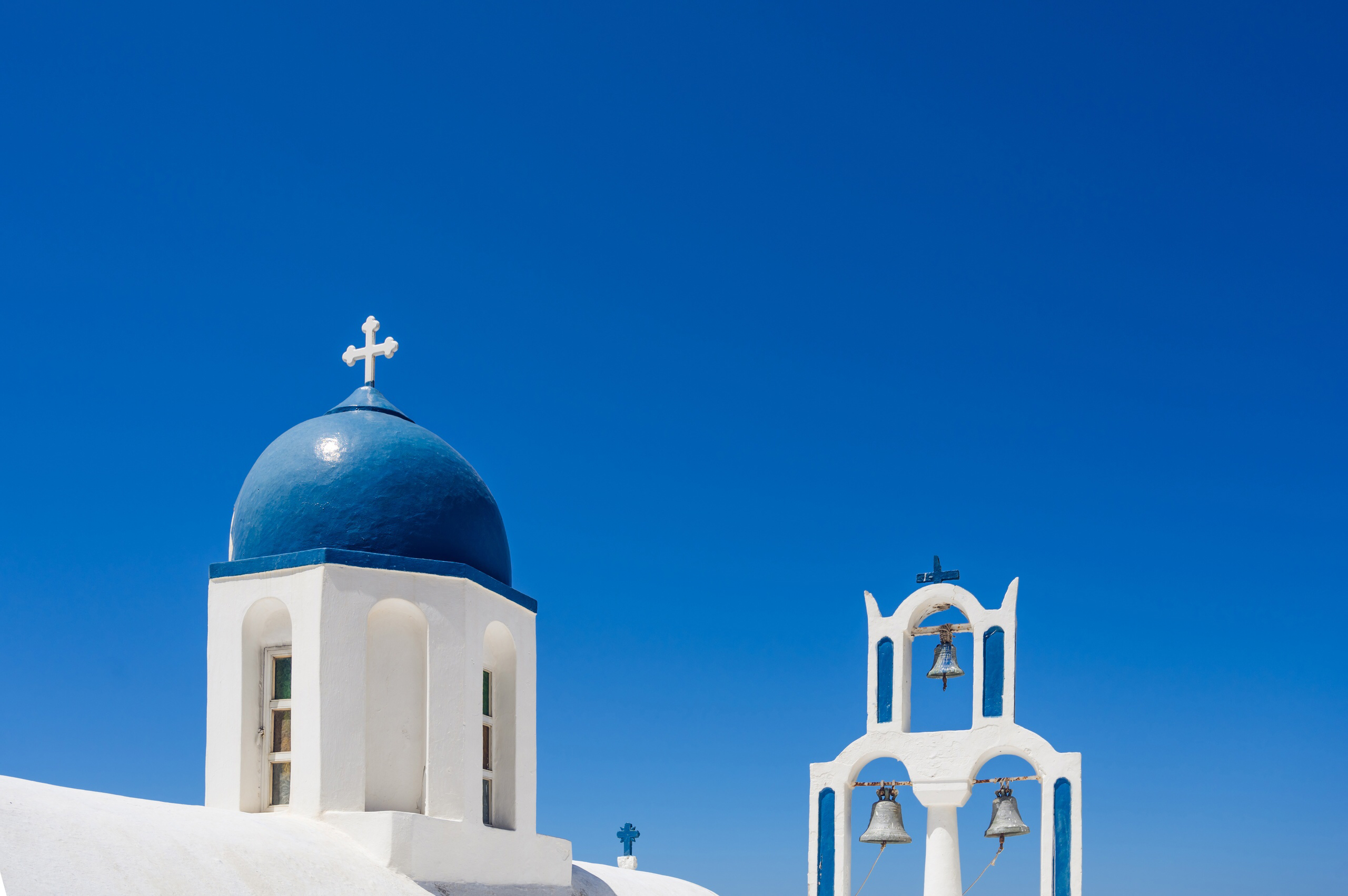 Iconic blue dome and bell tower of a church in Santorini under a clear blue sky.
