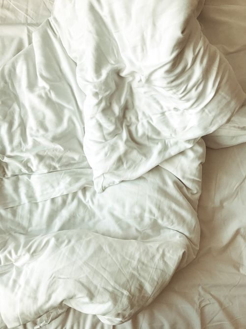 Free Close-up of soft, wrinkled white bed linen in a sunlit room, offering a cozy atmosphere. Stock Photo