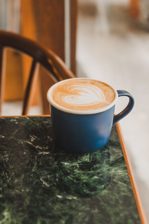 Free A blue coffee mug with heart-shaped latte art on a green marble table, capturing a warm, cozy vibe. Stock Photo