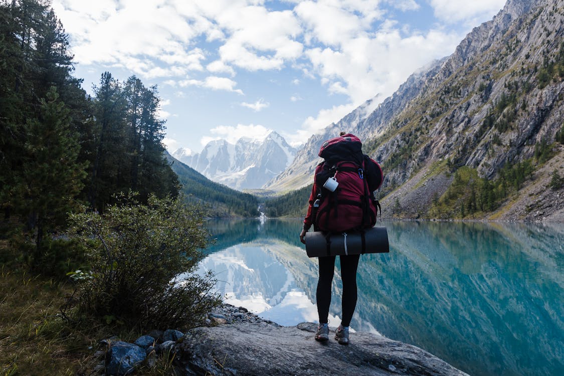 Free Person in Red Jacket and Black Pants Standing on Rock Near Lake Stock Photo