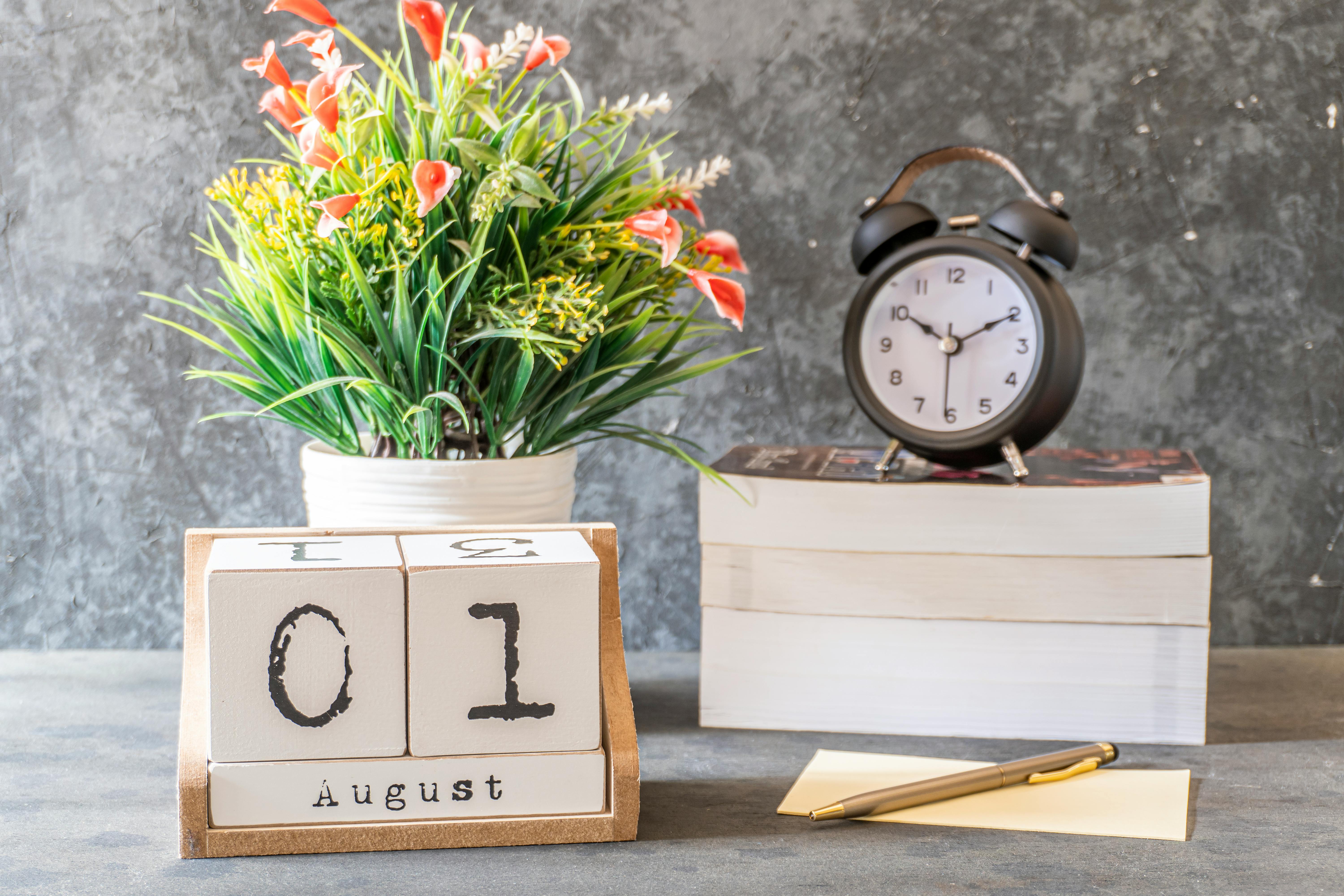 Elegant desktop setup with a calendar, clock, books, and a floral arrangement.