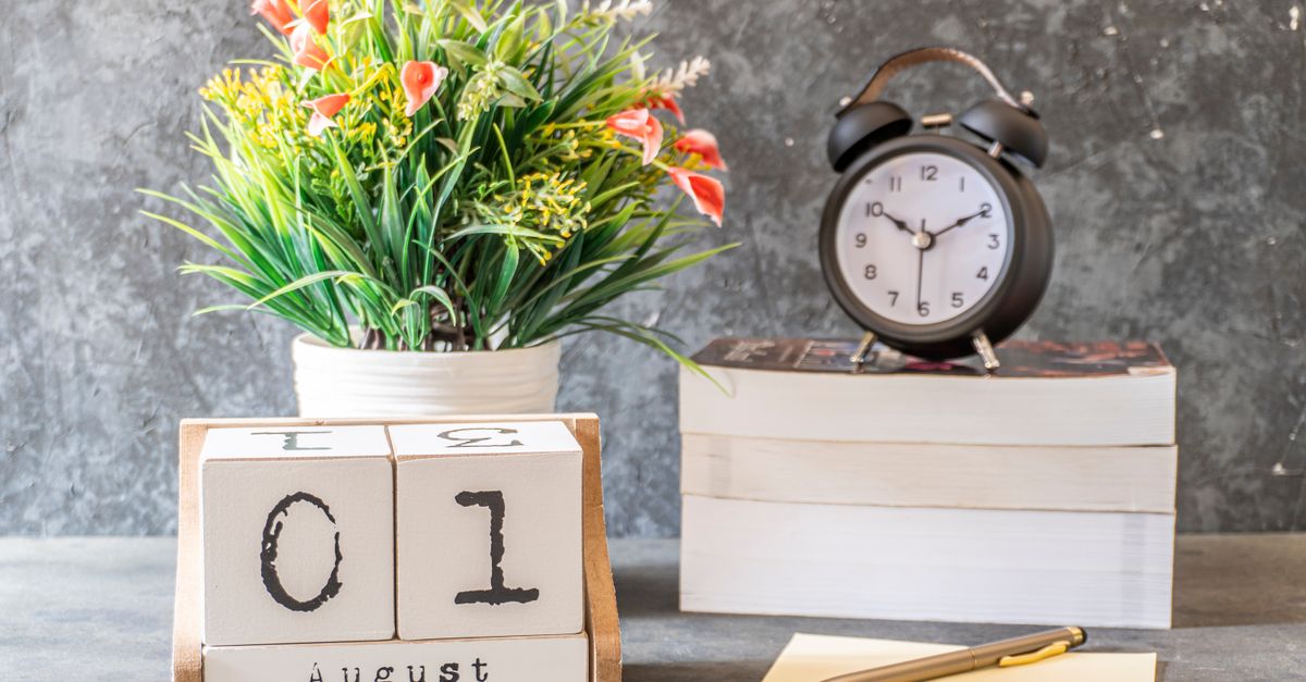 Elegant desktop setup with a calendar, clock, books, and a floral arrangement.