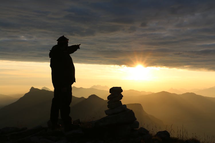 Silhouette Of Man Standing On Cliff During Sunset