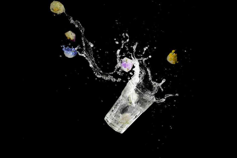 Fotomural Un vaso capturado en medio de un salpicón con flores congeladas vibrantes sobre un fondo negro.