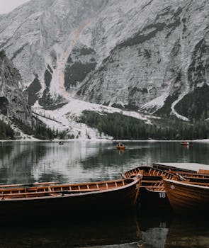 Peaceful mountain lake scene with wooden boats and snow-dusted peaks reflecting on the water.