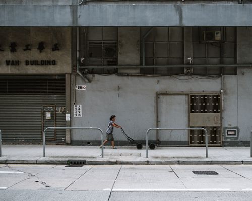 Free A woman pulling a cart along an urban street in downtown Hong Kong, capturing the city's hardworking spirit. Stock Photo