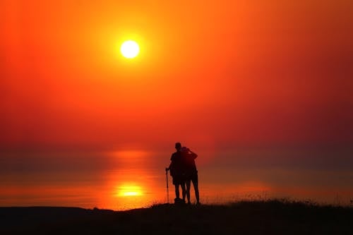 Free Silhouette of a Two People Standing on a Grassy Field near the Beach Stock Photo