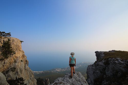 Free Back View of a Person with a Hat Standing on a Cliff Stock Photo