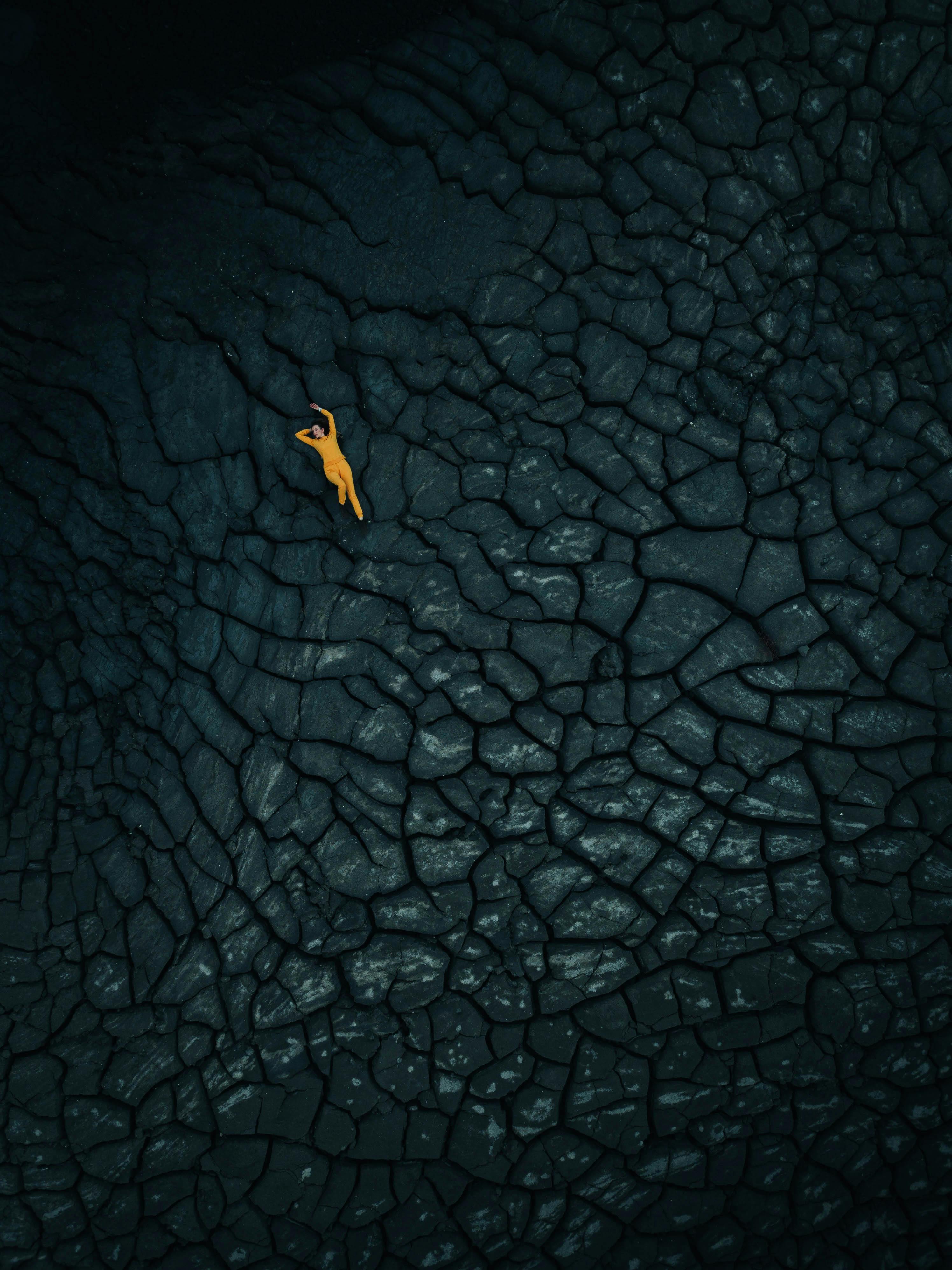 Aerial shot of a person lying on an arid, cracked earth surface, capturing the texture and forms of barren land.