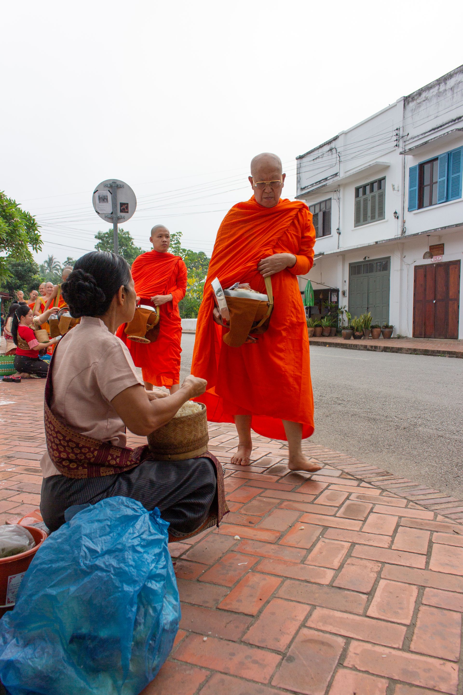 Monjes con túnica naranja recibiendo ofrendas al amanecer en Luang Prabang