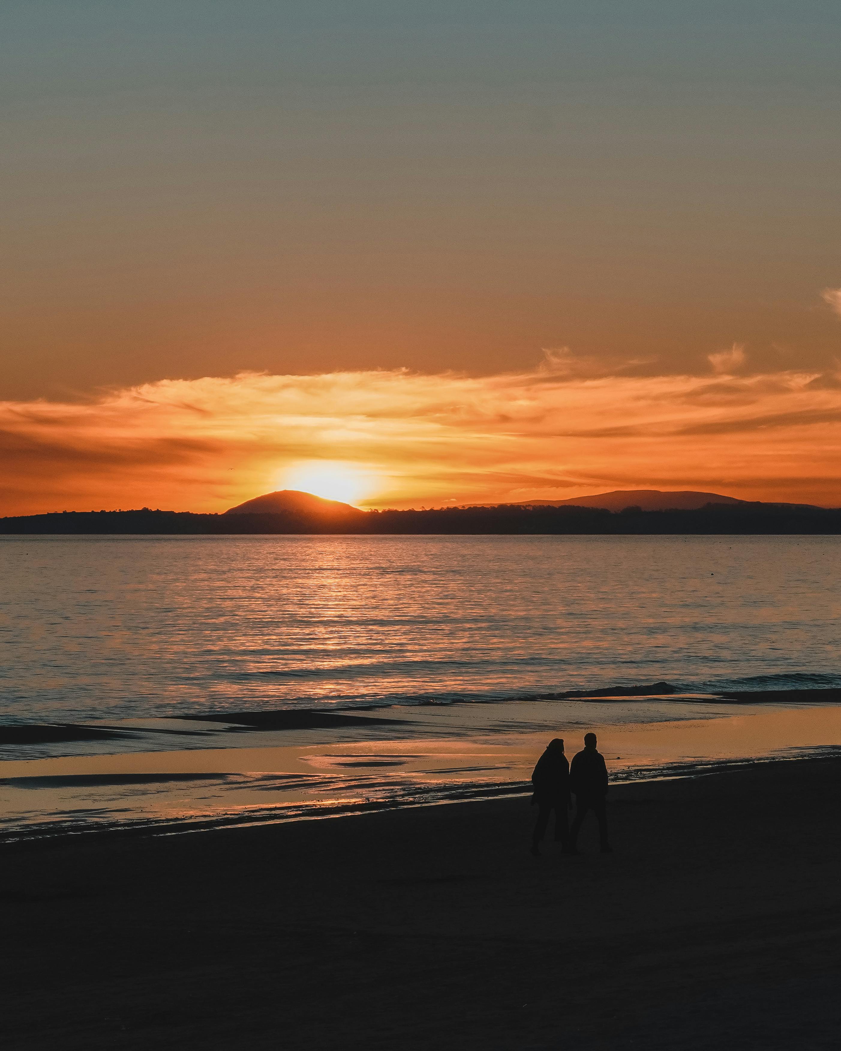 silhouette of two people walking on the beach