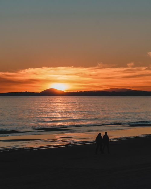 Free Couple walking on Punta del Este beach at sunset, showcasing vibrant skies and calm ocean. Stock Photo