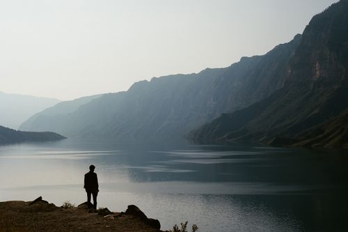 Free A solitary figure stands by the calm waters of Sulak Canyon in Dagestan, Russia, under a serene sky. Stock Photo