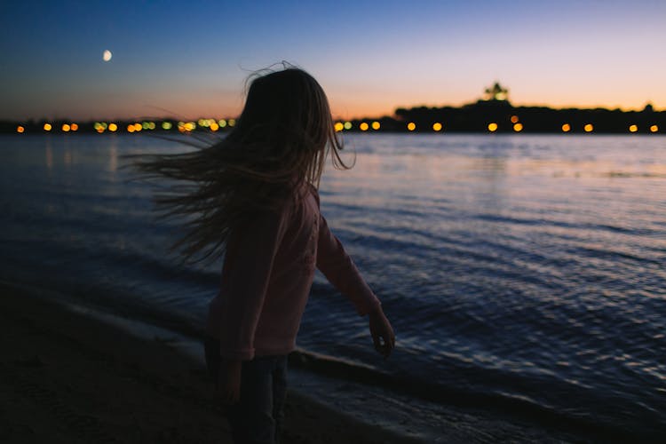 A Girl In A Pink Long Sleeve Shirt Standing On Beach During Sunset