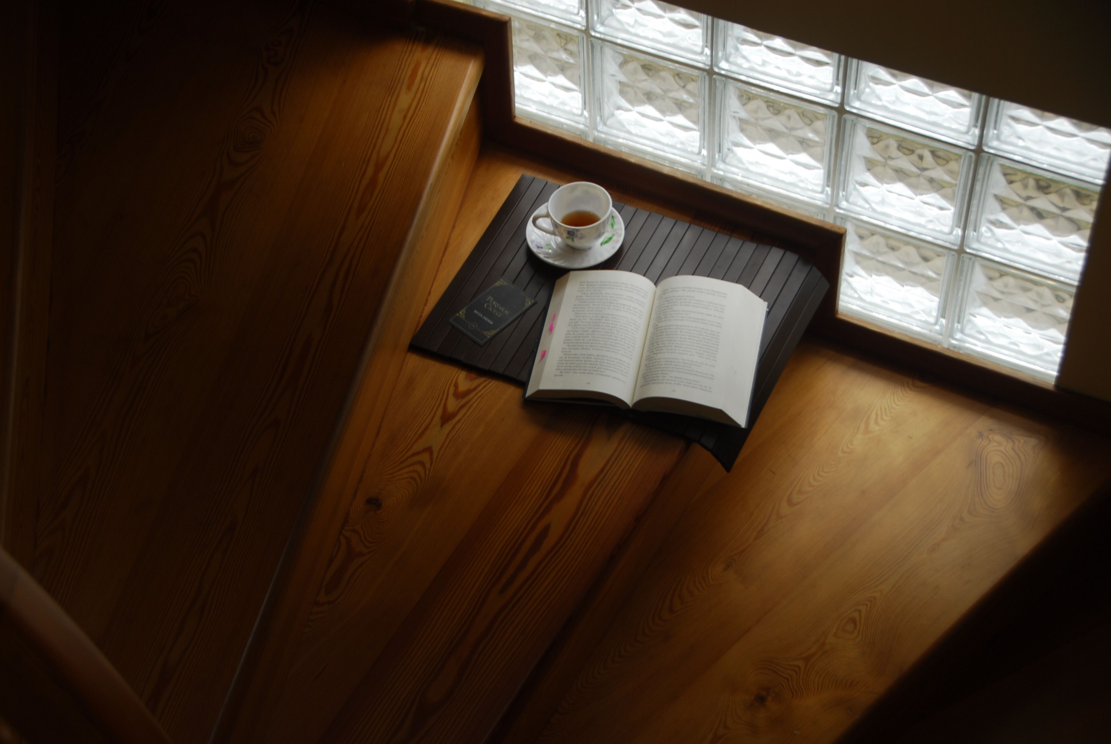 A serene setting with an open book and tea cup on a wooden staircase by a window.