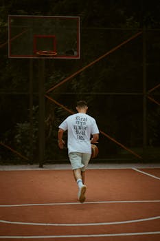 A teenager dribbles a basketball on an outdoor court, showing youthful energy and focus.