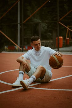 Casual young man relaxing on an outdoor basketball court with a basketball in hand.