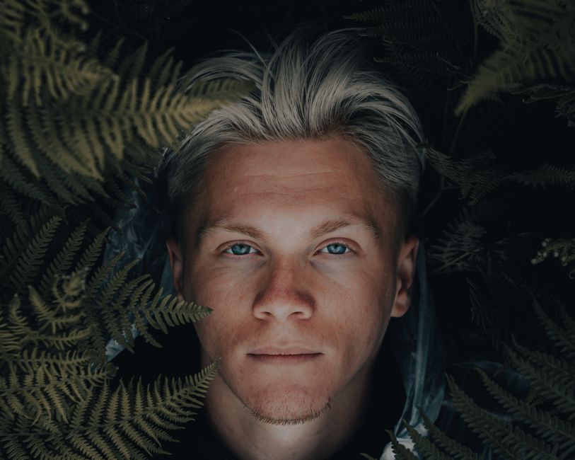 Close-up portrait of a young man with ferns, highlighting natural beauty and serenity.