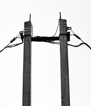 Monochrome image of electric utility poles silhouetted against a clear sky.