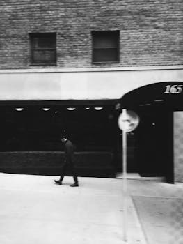 Black and white street photo of a person walking in a city setting, capturing urban life.