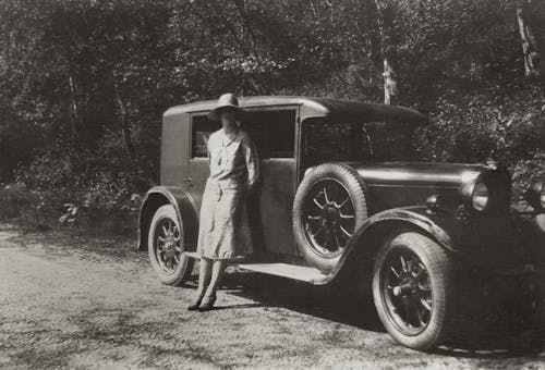 Woman in Dress Standing Beside Vintage Car Along Roadside