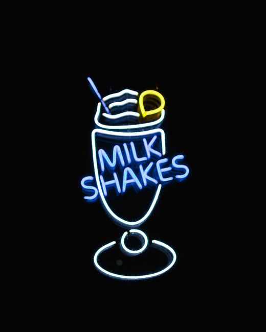 Bright neon sign of a milkshake glowing against a dark background, perfect for diner and retro vibes.