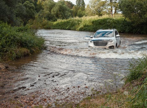 An SUV crosses a shallow river surrounded by lush greenery, showcasing off-road capabilities.