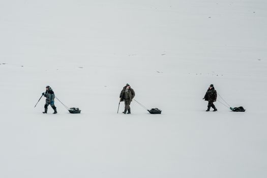 Three adults with sleds trekking across a snowy landscape, showcasing winter adventure and exploration.