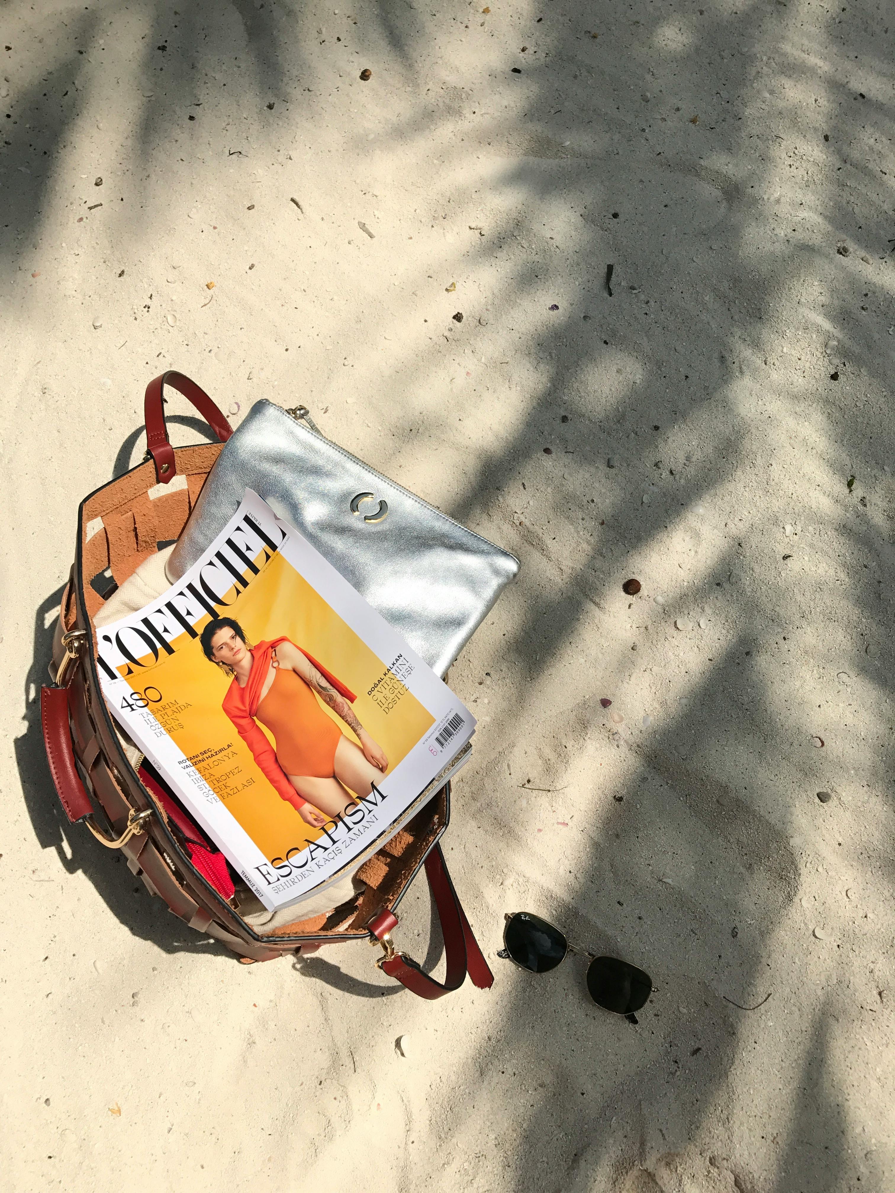 A stylish beach bag with a magazine, sunglasses on sandy terrain in Tanzania.