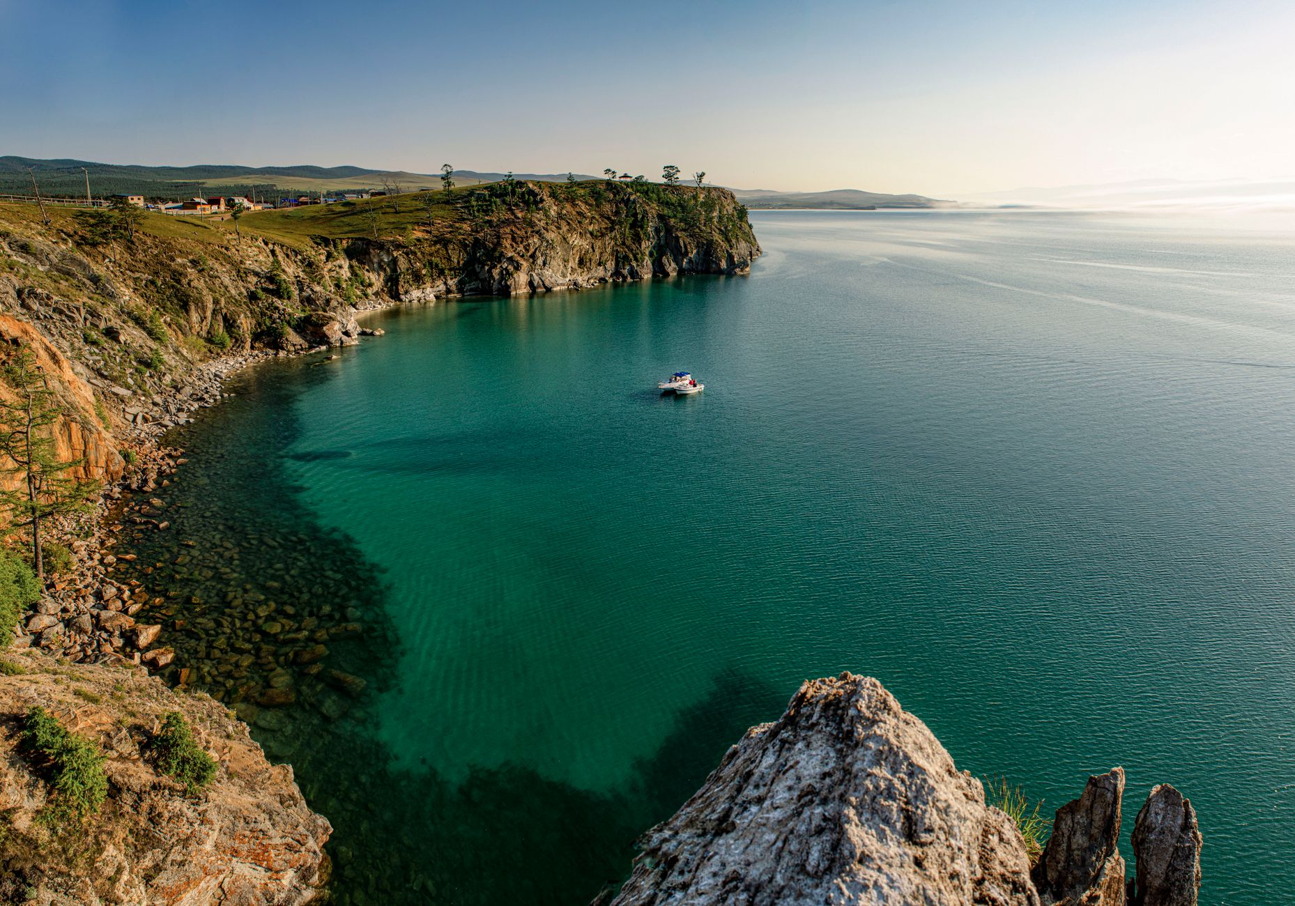 A scenic aerial view of a tranquil coastal bay with clear blue waters and a solitary boat, surrounded by rugged cliffs.