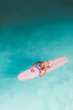Captivating aerial shot of a female surfer on a pink surfboard navigating clear turquoise waters.