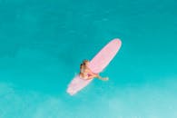 一名女子在晶莹剔透的蓝色海水中享受粉红色冲浪板冲浪