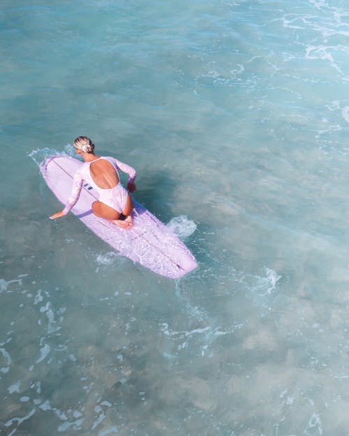 Photograph of a Woman in a Pink Swimsuit Kneeling on a Surfboard