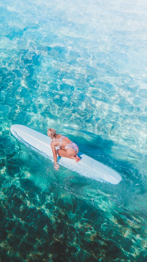 Photo of a Woman in a Bikini Kneeling on a Surfboard