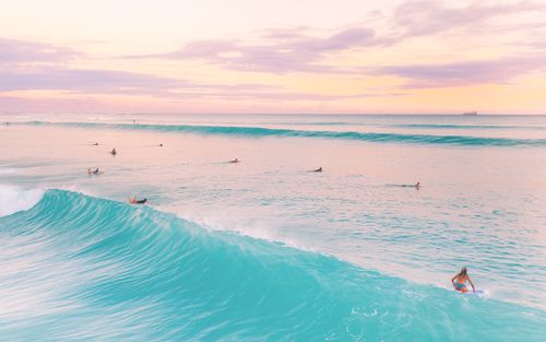 Free A stunning scene of surfers catching waves in a serene ocean at sunset, showcasing vibrant colors. Stock Photo
