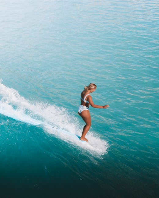 A woman skillfully surfs on a vibrant blue ocean wave, showcasing an exhilarating outdoor adventure.