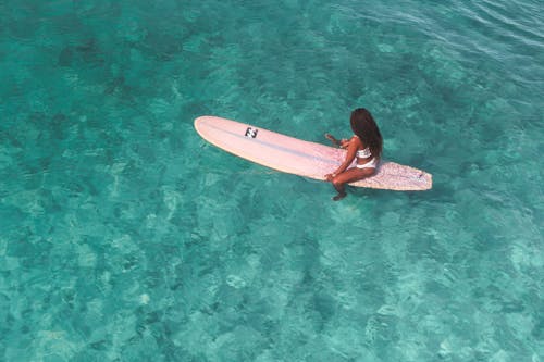 Woman in a White Bikini Sitting on a Surfboard