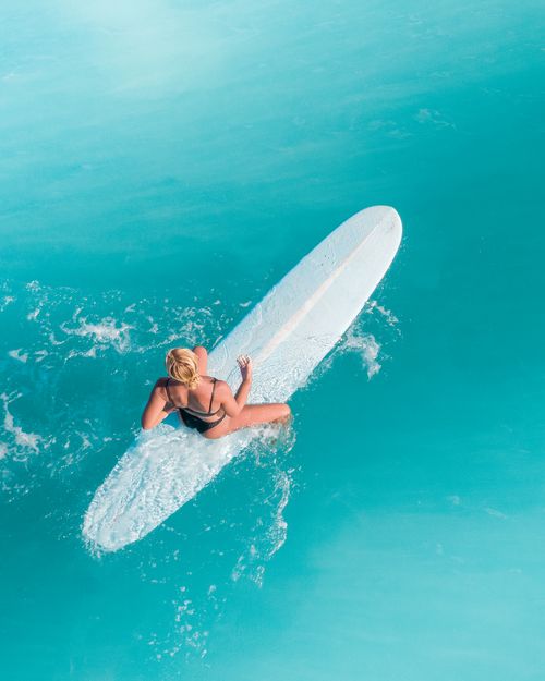 Free High-angle shot of a woman in swimwear surfing on a turquoise ocean. Stock Photo