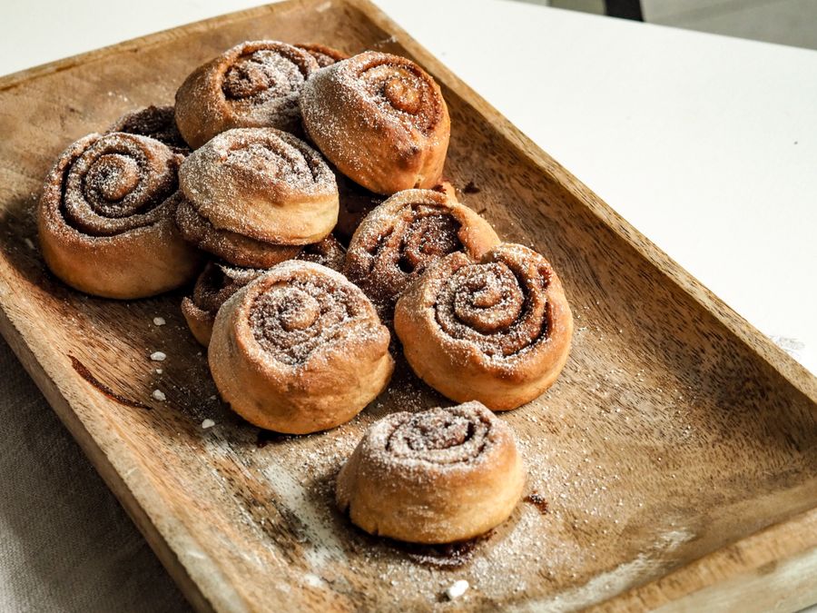 A batch of freshly baked cinnamon rolls dusted with sugar on a wooden tray.