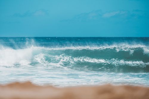Free Captivating ocean waves crashing against a sandy beach under a clear blue sky. Stock Photo