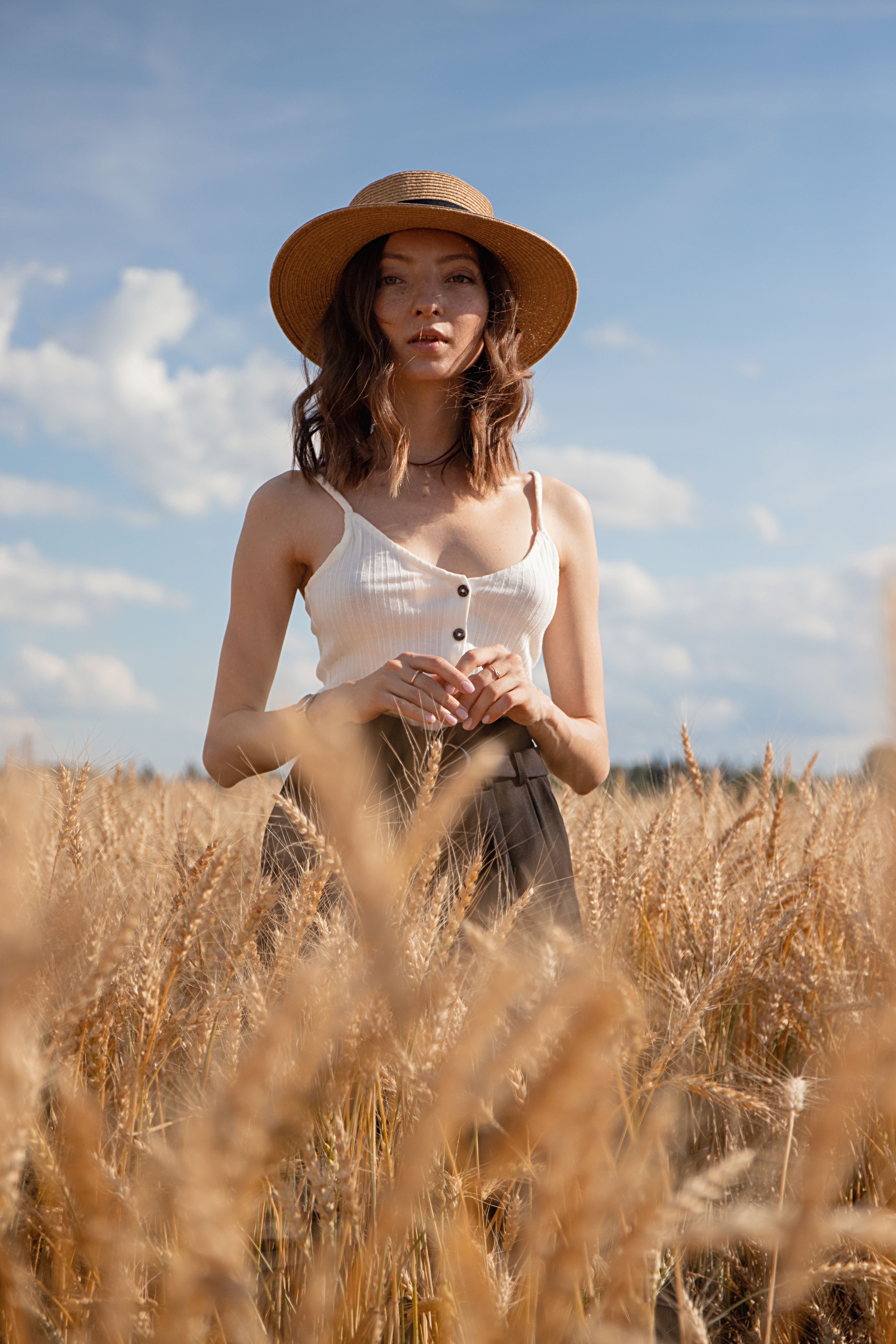 Young woman wearing a sun hat, standing confidently in a golden wheat field under a blue sky.