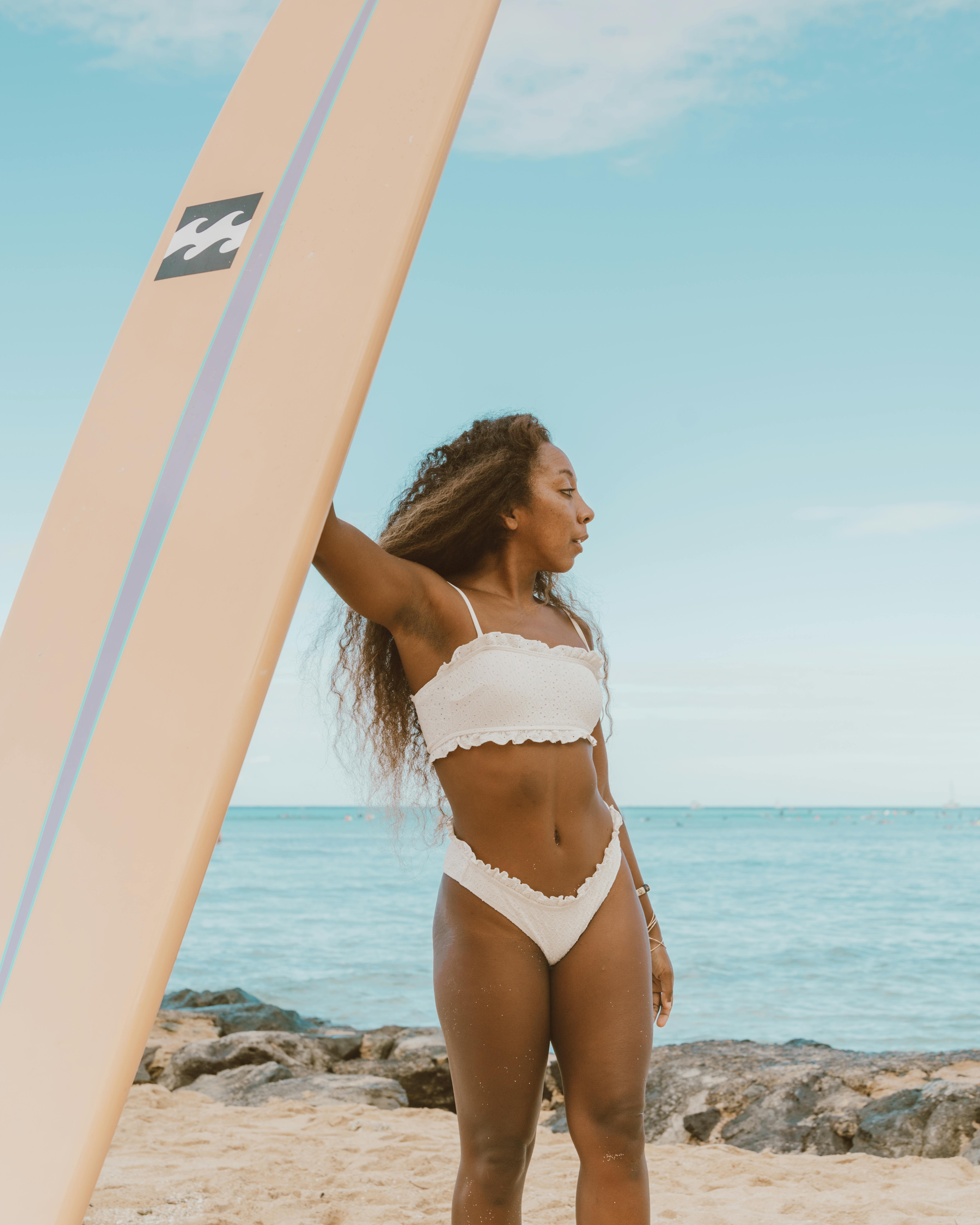 一位自信的女性在阳光明媚的海滩上拿着冲浪板，拥抱户外冒险